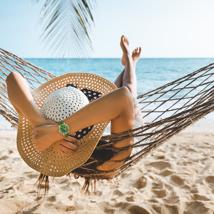 Frau entspannt in einer Hängematte am Strand und trägt die Chocomoon Damenuhr Palmtrees mit tropischem Blätterdesign