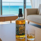 The Matsui Mizunara Cask Japanese Single Malt Whisky auf einem Holztisch mit Glas, im Hintergrund Meerblick und moderne Einrichtung